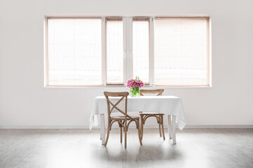 Vase with flowers on table and chairs in big empty room