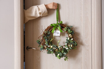 Woman hanging Easter wreath on wooden door, closeup