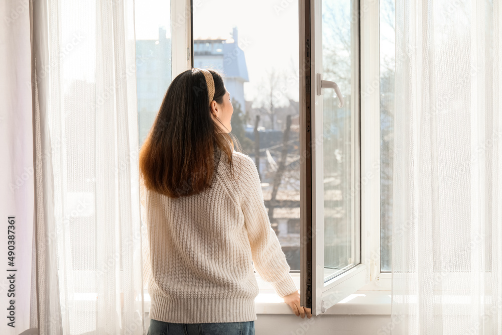 Wall mural Pretty young Asian woman near open window at home