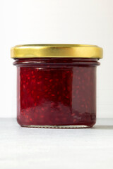 Packaging for jam. Raspberry jam in glass jar close-up on white background. Vertical layout.