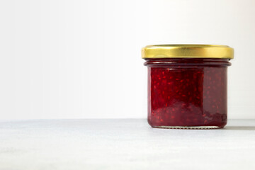 Raspberry jam in glass jar close-up on white background copy space.