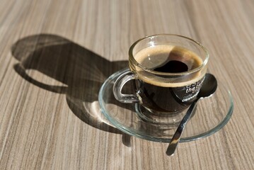 Transparent Cup of Coffee with Shadow on Wood Table in Switzerland.
