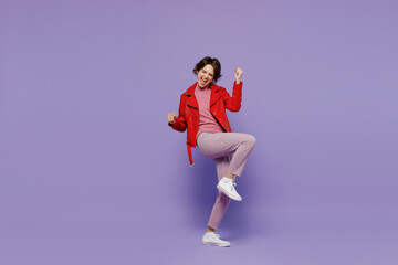 Full body young smiling happy woman 20s in red leather jacket doing winner gesture celebrate clenching fists say yes isolated on plain pastel light purple background. People lifestyle fashion concept.