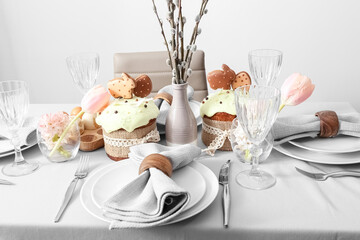Beautiful table setting with Easter cakes, flowers and willow branches in room