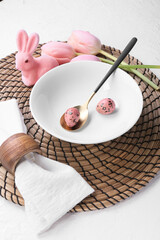 Beautiful table setting with Easter eggs, rabbit and tulips on white background