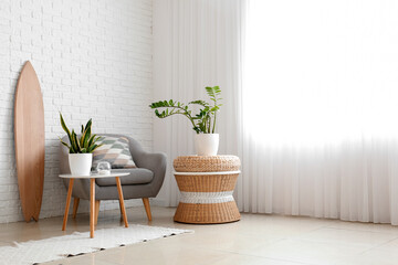 Interior of light living room with wooden surfboard, armchair and houseplants