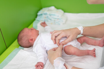 hands of a mom who just gave birth in the maternity hospital with the hospital identification bracelet and the medication line on her wrist puts a bodysuit on her newborn baby after changing her diape