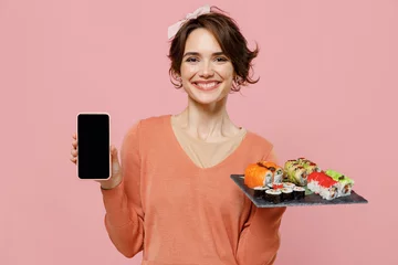 Cercles muraux Bar à sushi Young fun woman in casual clothes hold makizushi sushi roll served on black plate traditional japanese food use mobile cell phone blank screen workspace area isolated on plain pastel pink background