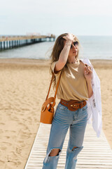 Young blonde woman in casual clothes, jeans on the background of a beautiful blue sea. Vacation spring concept