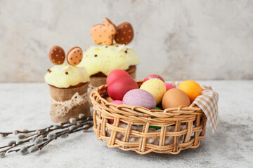 Gift basket with painted Easter eggs, pussy willow branches and cakes on light background