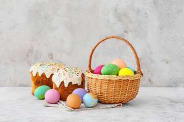Gift basket with painted Easter eggs and cakes on light background