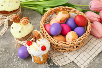 Obraz na płótnie Canvas Gift basket with painted Easter eggs and cakes on grey background