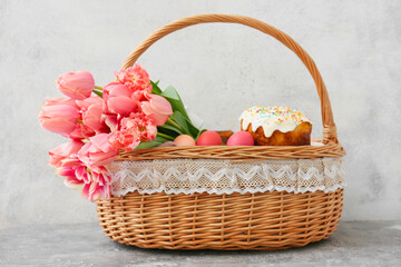 Gift basket with painted Easter eggs, tulip flowers and cake on table