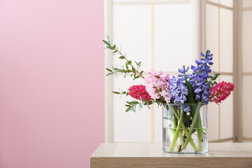 Vase with spring flowers on table and folding screen near pink wall