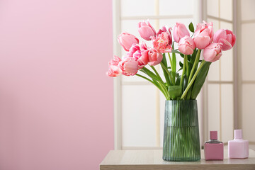Vase with pink tulips and bottles of perfume on table in room