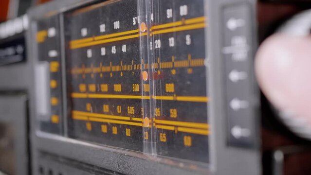 Female Fingers Adjusting the Frequency on an Old Vintage Analog Receiver. Search for a music radio station on a dial scale on panel of a short-wave portable FM radio, player, tape recorder 80s, 90s.