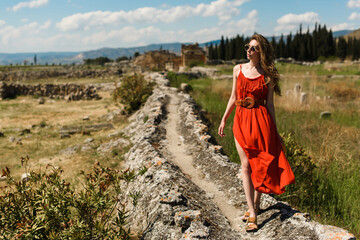 A young beautiful woman in a red dress walking in Pamukkale, Turkey, against the backdrop of the...
