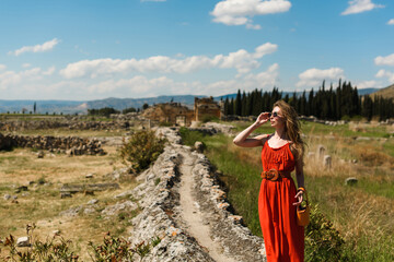 A young beautiful woman in a red dress walking in Pamukkale, Turkey, against the backdrop of the...