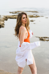 Fashion portrait of a young sexy caucasian woman in a stylish swimsuit and white shirt on the background of sea waves