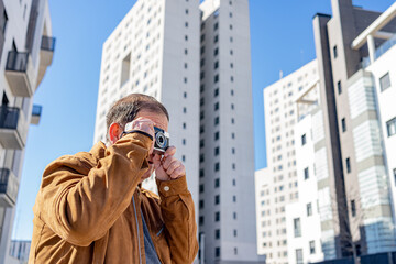 Older man photographing with an old film camera in the city.