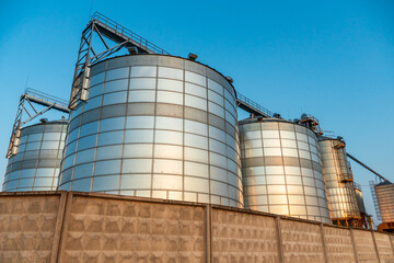 A large modern plant for the storage and processing of grain crops. view of the granary on a sunny day. Large iron barrels of grain. silver silos on agro manufacturing plant for processing and drying