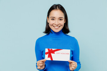 Fototapeta na wymiar Fascinating fun smiling young woman of Asian ethnicity 20s years old wear blue shirt hold gift certificate coupon voucher card for store isolated on plain pastel light blue background studio portrait
