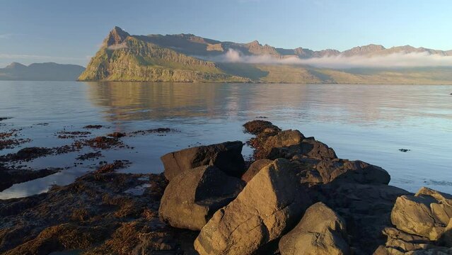 Early morning at the shore of Mj&oacute;ifj&ouml;r&eth;ur, East fiords of Iceland. Slow moving push-in shot over rocks at waters edge, Mountain in background.
