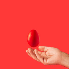 A unique composition from real life, a beautiful male hand catches a red egg for Easter 2022