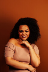 pretty young african american woman with curly hair posing cheerful gesturing on brown background, lifestyle people concept