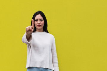 Displeased asian woman standing with hand on hip and pointing with finger while showing no sign on...