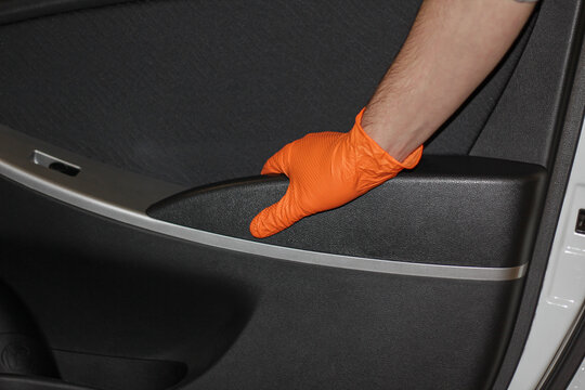 The man's hand opening the car door, the hand holding the car door handle. A man's hand in a rubber glove is holding the handle of the car door opener.