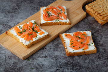 Home made bread on a wooden cutting board with curd cheese, salmon and herbs