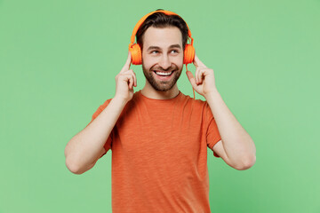 Young smiling fun satisfied cool man 20s wear casual orange t-shirt headphones listen to music dancing isolated on plain pastel light green color background studio portrait. People lifestyle concept.