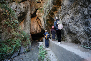 A rear view of hikers walking by the narrow pathway through the rocky hills