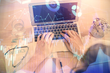 Double exposure of man's hands typing over laptop keyboard and forex chart hologram drawing. Top view. Financial markets concept.