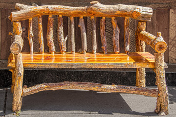 Rustic wooden bench made of rough logs with bark sitting on sidewalk against wooden wall on sidewalk
