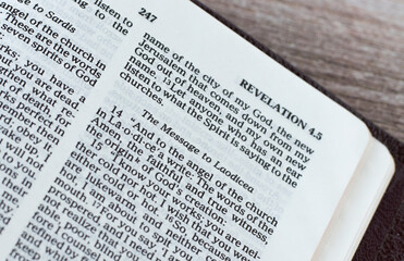 The message to Laodicea Church from God Jesus Christ, an open Holy Bible Book Revelation on wooden background. Christian biblical concept of warning to believers. A close-up.	