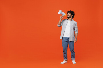 Full size body length promoter young bearded Indian man 20s years old wears blue shirt hold scream in megaphone announces discounts sale Hurry up isolated on plain orange background studio portrait. - obrazy, fototapety, plakaty
