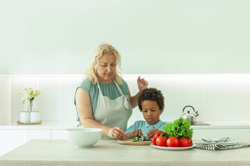 Portrait of woman and her child son preparing food together standing at a worktop in white kitchen background