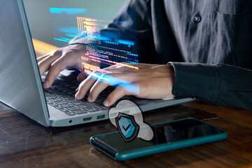 Obraz na płótnie Canvas Homem digitando no teclado do laptop com celular ao lado com simbolo de segurança no telefone e gráficos de algoritmos no teclado com sobre posição de imagem