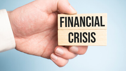 Text FINANCIAL CRISIS on wooden blocks on a wooden table. Hands of businesswoman as the background. Financial concept.