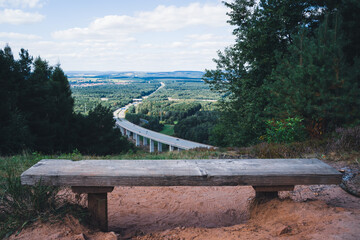 Wooden bench overlooking a highway bridge between tress in the forest