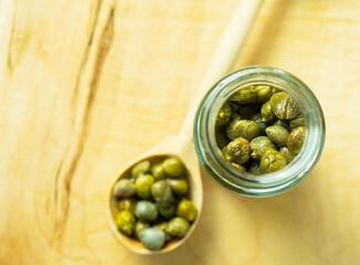 Capers in a glass jar. Pickled capers in a jar on a wooden board top view