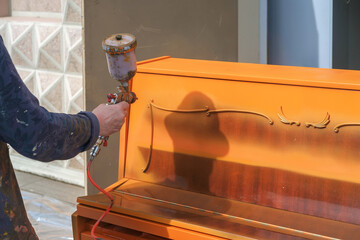 A Man's hand holding a paint spray gun and coloring a piano in an orange color