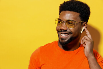 Young man of African American ethnicity 20s in basic casual orange t-shirt glasses listen music in...