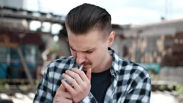 young handsome man with mustache in checkered black and white shirt smoking a cigarette outside. bad habit.