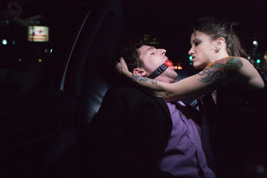 Dominatrix and man wearing ball gag in limousine