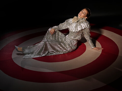 Portrait of a woman in a silver dress sitting on a large hand painted Bulls-eye target