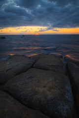 Rocky shore with stones sinking in the sea water. Sunset, long exposure. Baltic sea.