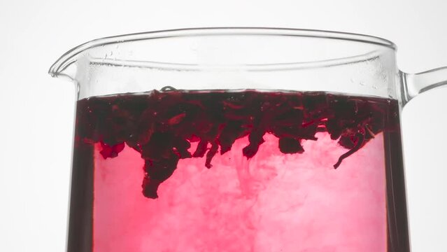 Hibiscus Brewed in Boiling Water. Time Lapse. Dried hibiscus petals float on the surface of the hot water in the kettle and intensely stain it a rich pink color
